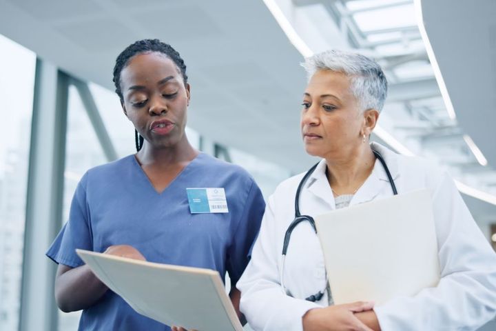 A nurse has a discussion with a physician, as they both look at a patient's chart.