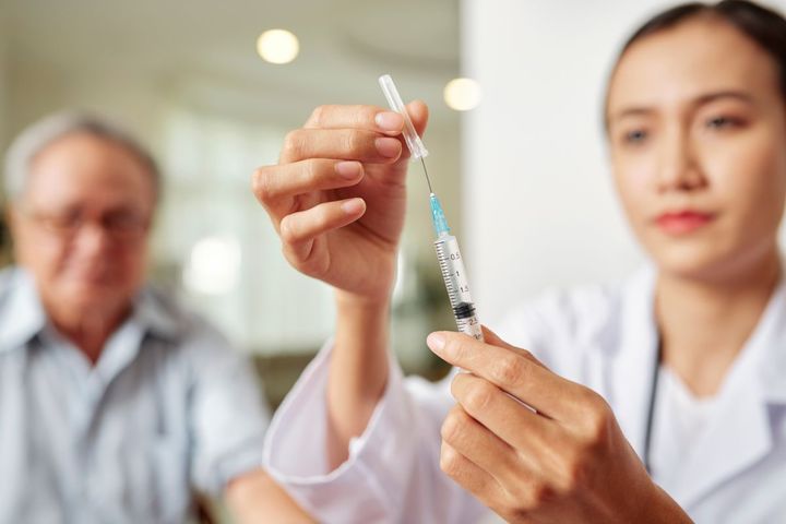 Female clinician taking cap off of syringe next to patient