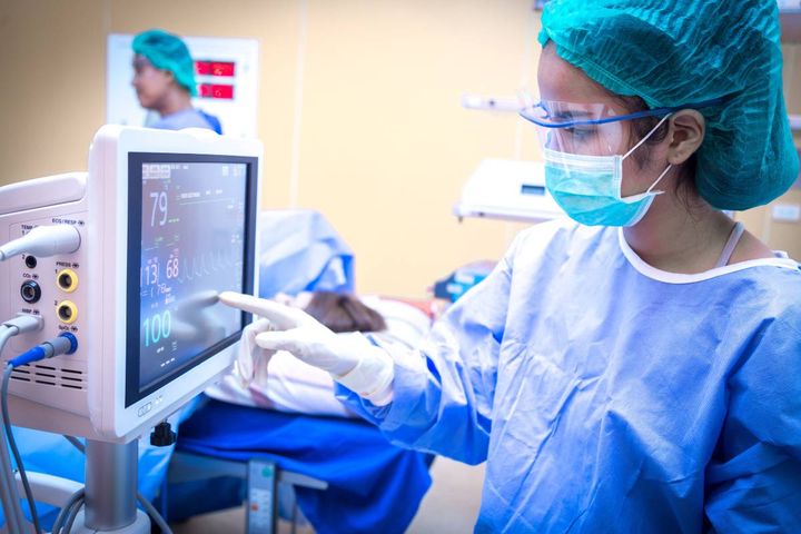 A nurse with CNAMB certification checks a monitor during a surgical procedure.
