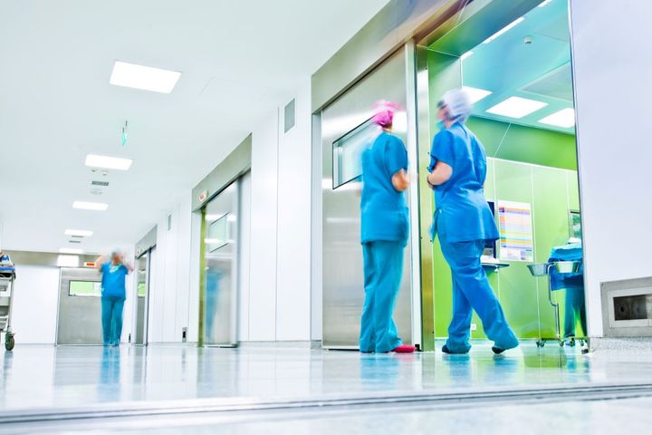 Wide shot of a hospital hallway, showing a few nurses.