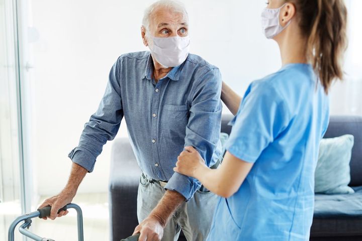 A nurse helps an elderly man safely use a walker.
