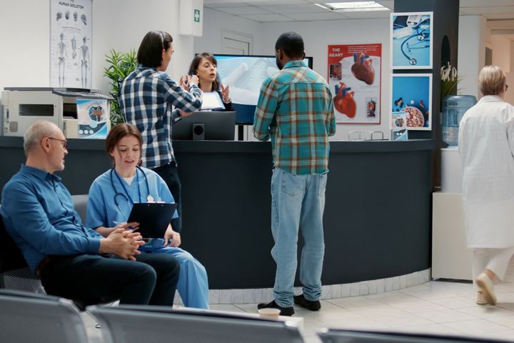 A busy doctor's office, with many patients, nurses, and administrators.