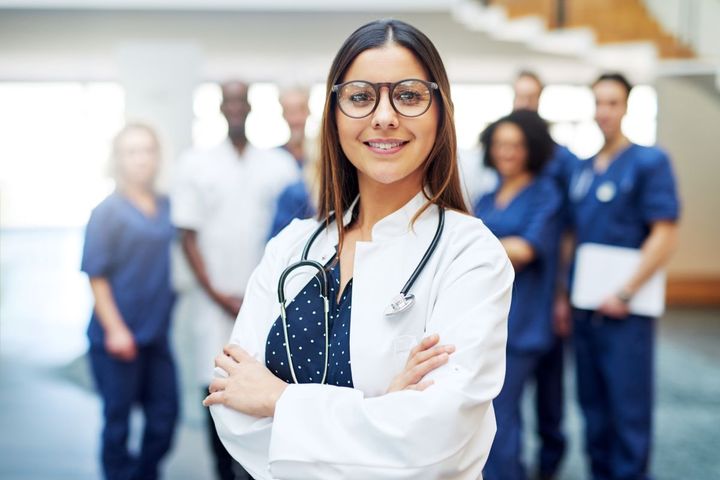 A physician in the foreground smiles at the camera.