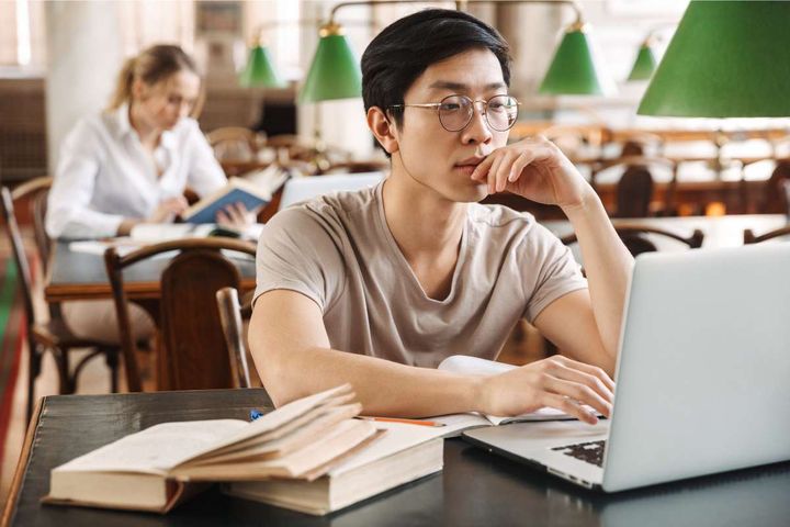 Asian male medical librarian researching on a laptop in a library.
