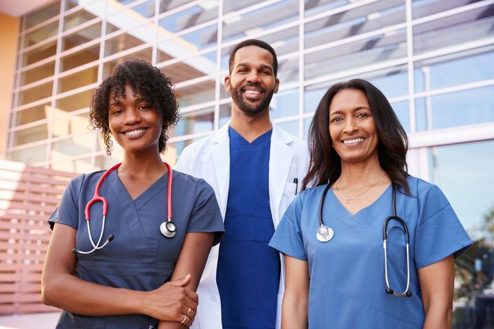 A group of three nurses poses for a picture outside of their facility.