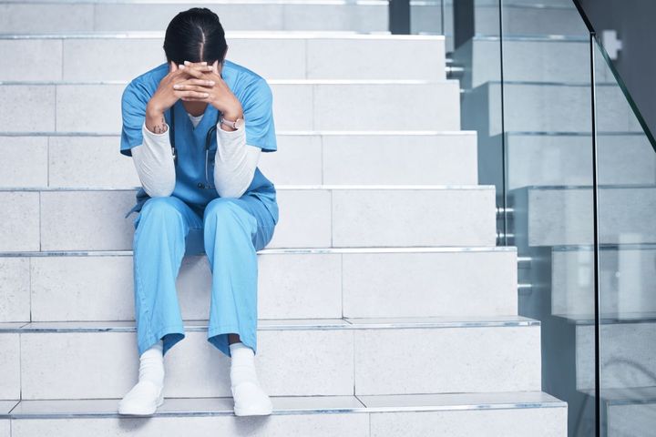 A nurse sitting on the stairs, with her head despondently in her hands.