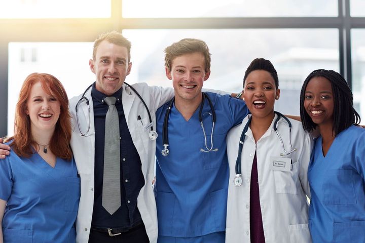 A group of nurses and physicians embrace and smile for the camera.