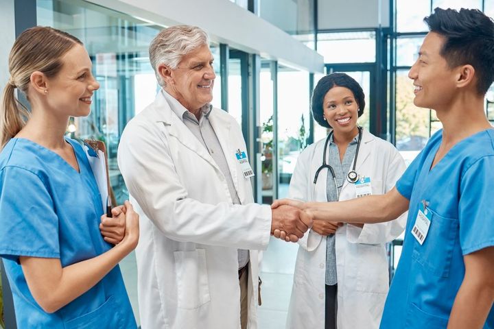 A newly hired nurse meets a fellow nurse and doctor, and shakes hands with a doctor.