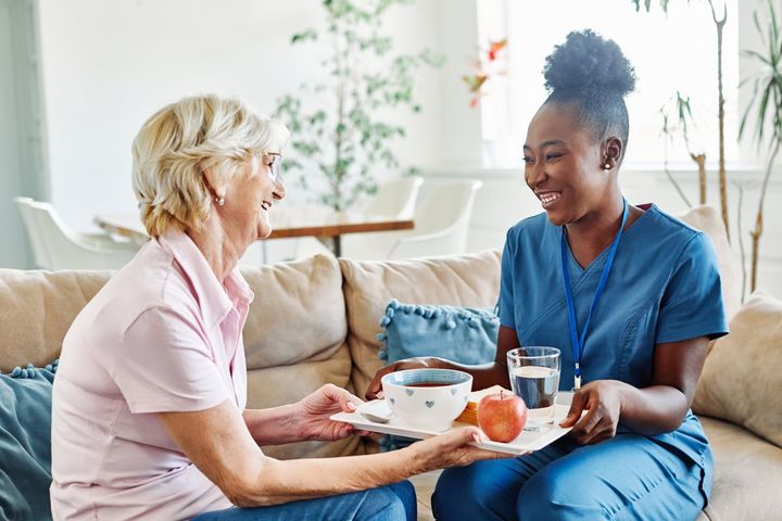 A nurse at a long term care facility serves lunch and spends time with a resident.
