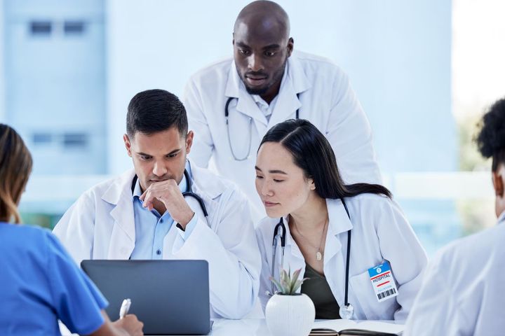 Three healthcare workers reading a healthcare ombudsman's report on a laptop screen.