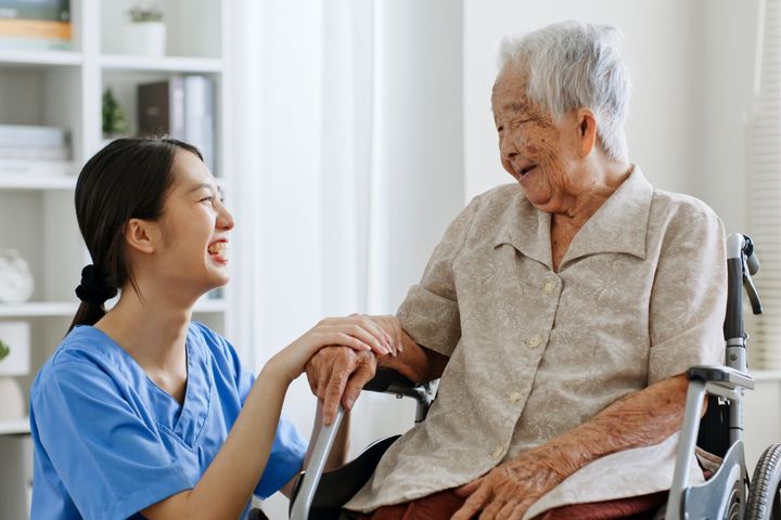 A nurse sits with one of her nursing home residents, who is in a wheelchair.
