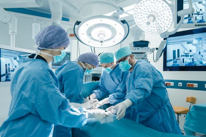 A surgeon, OR nurse, and other surgery staff work on a patient.