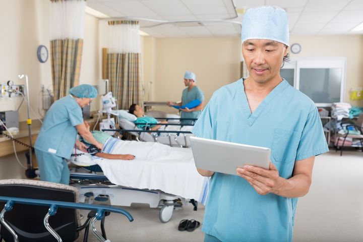 A PACU nurse checks his tablet next to a patient's bed.