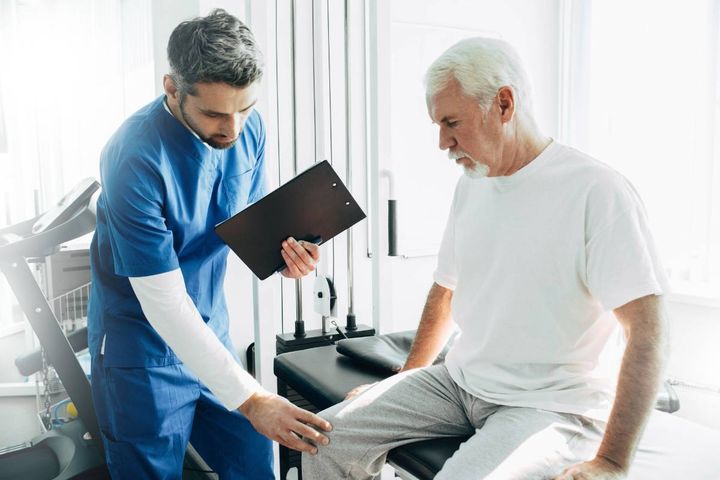 A rheumatology nurse practitioner assesses a patient's knee for arthritis.