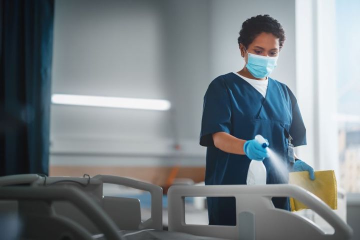 A hospital worker uses an antiseptic spray to clean a hospital bed, one of many standard precautions used to prevent infection.