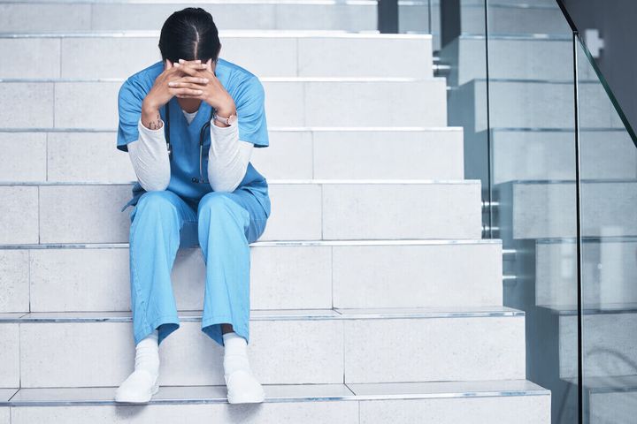 Stressed nurse sitting on steps and hiding face with hands.