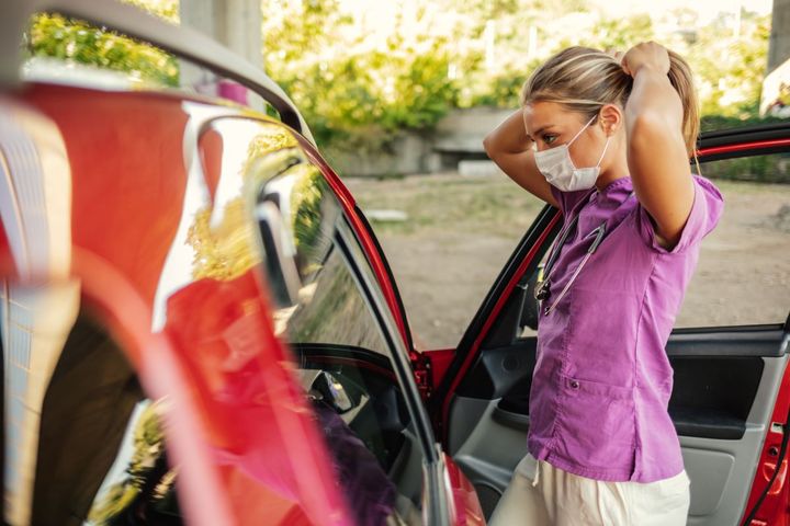 A nurse getting out of her car, fulfilling her duties in accordance with a travel nurse contract.