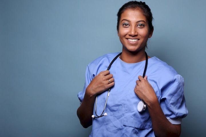 Nurse in scrubs holding stethoscope around her neck and smiling.