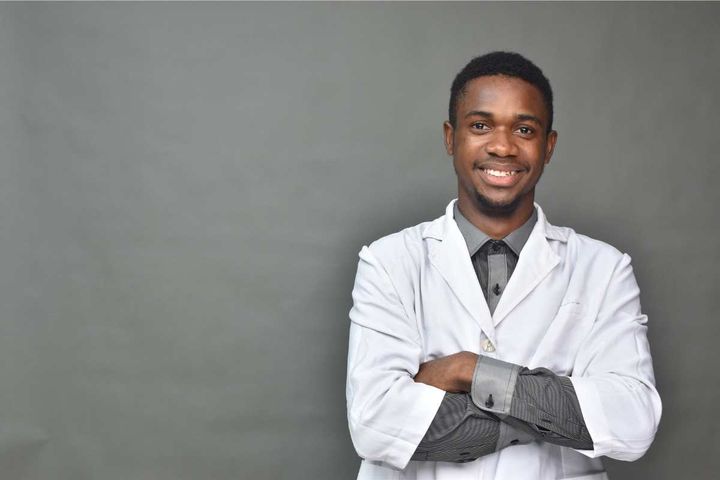 Young African American man in a white coat with his arms folded and smiling.