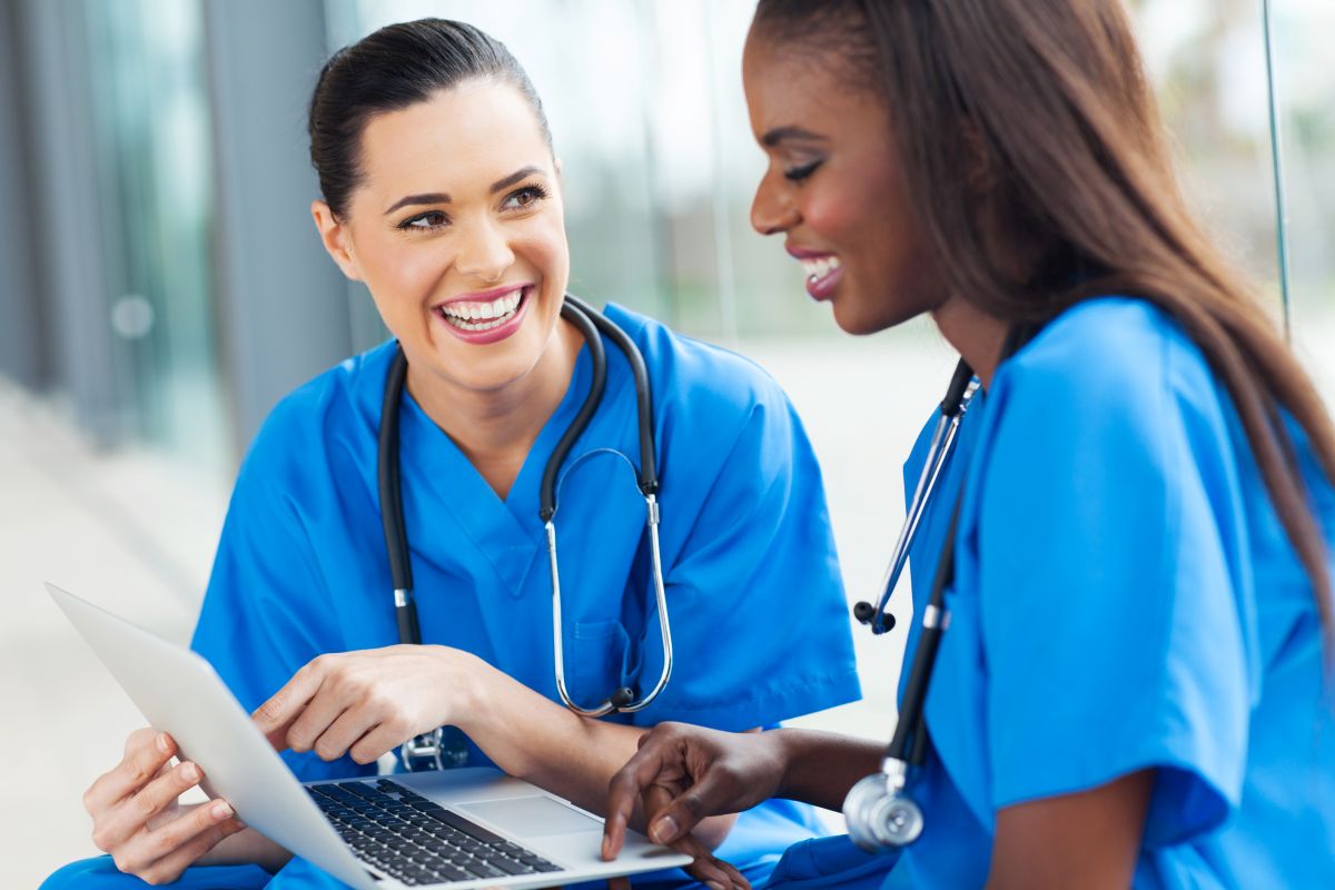 Two nurses, looking at a laptop computer and talking.