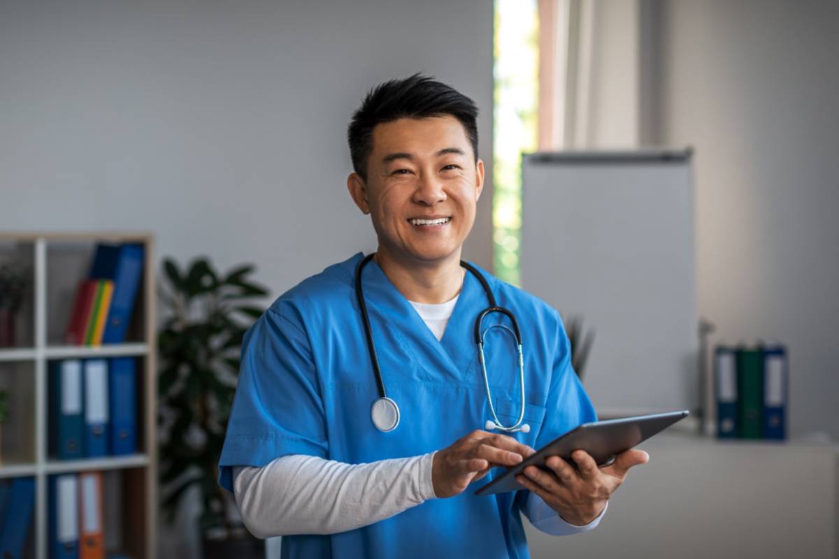 A nurse in blue scrubs smiles as he fills out paperwork for his ambulatory care nursing certification.