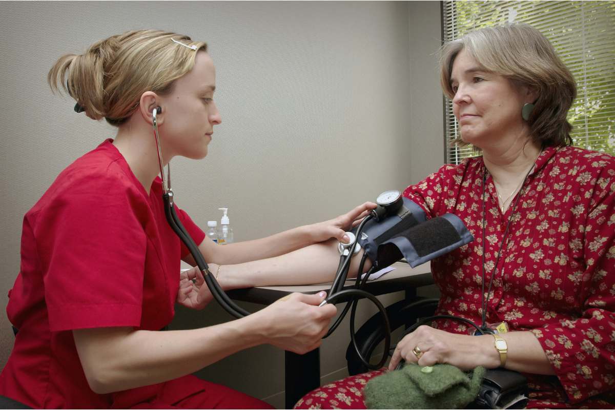 Nurse in red scrubs taking the blood pressure of a patient.