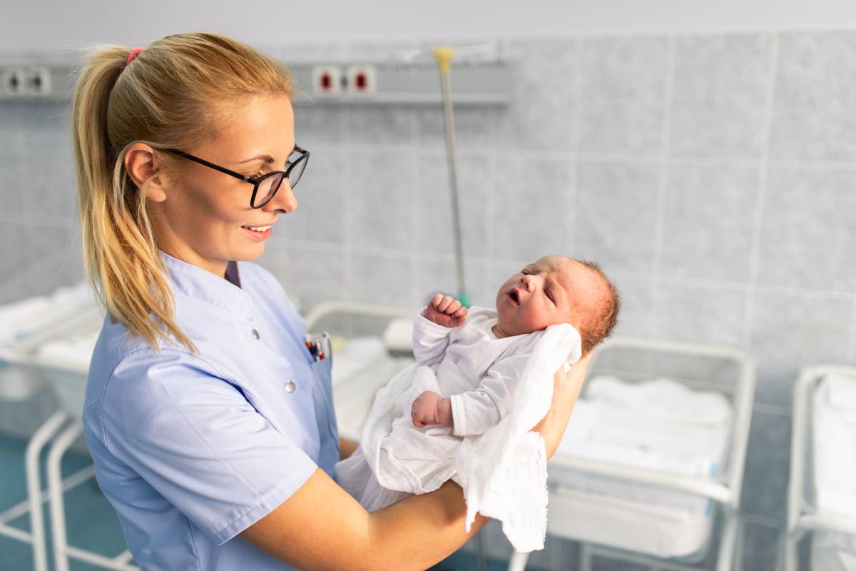 A nurse with C-EFM certification holds a baby in the hospital.