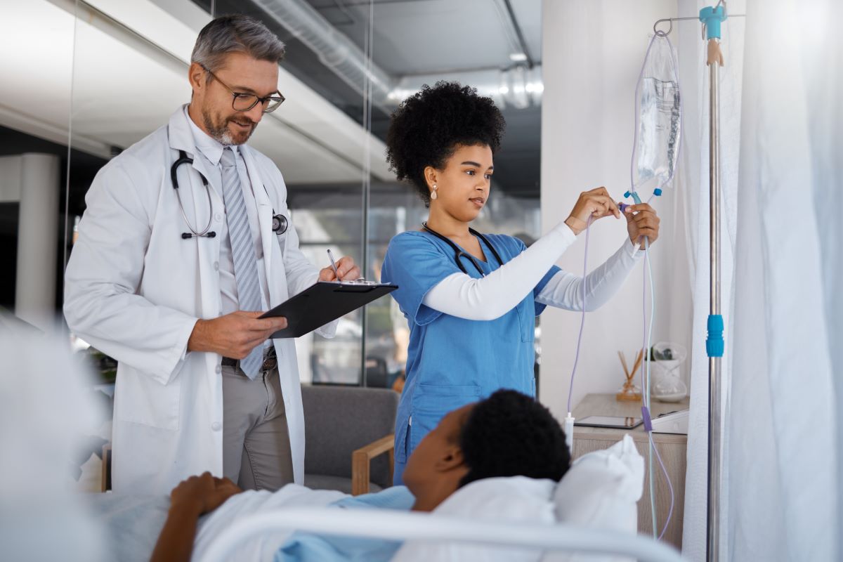 A nurse sets up an IV for a patient, while the physician checks his notes.