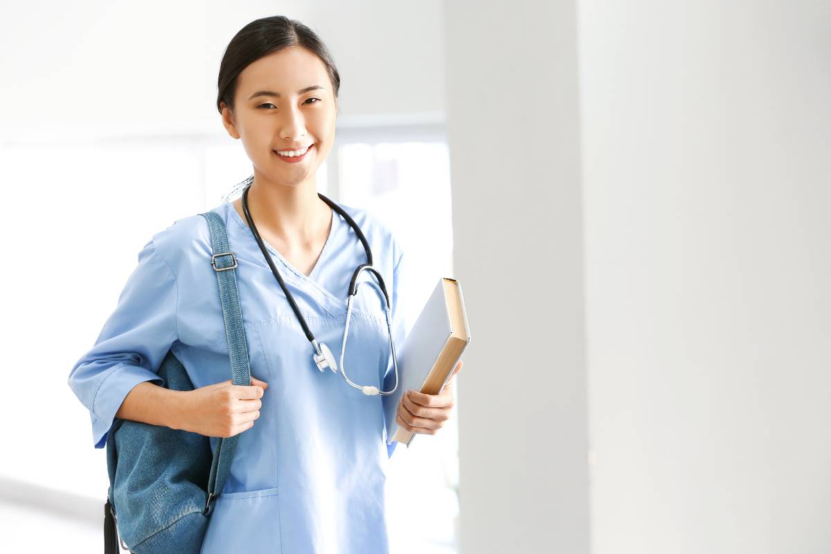 A nurse with CDDN certification poses for a photo with a book and backpack.