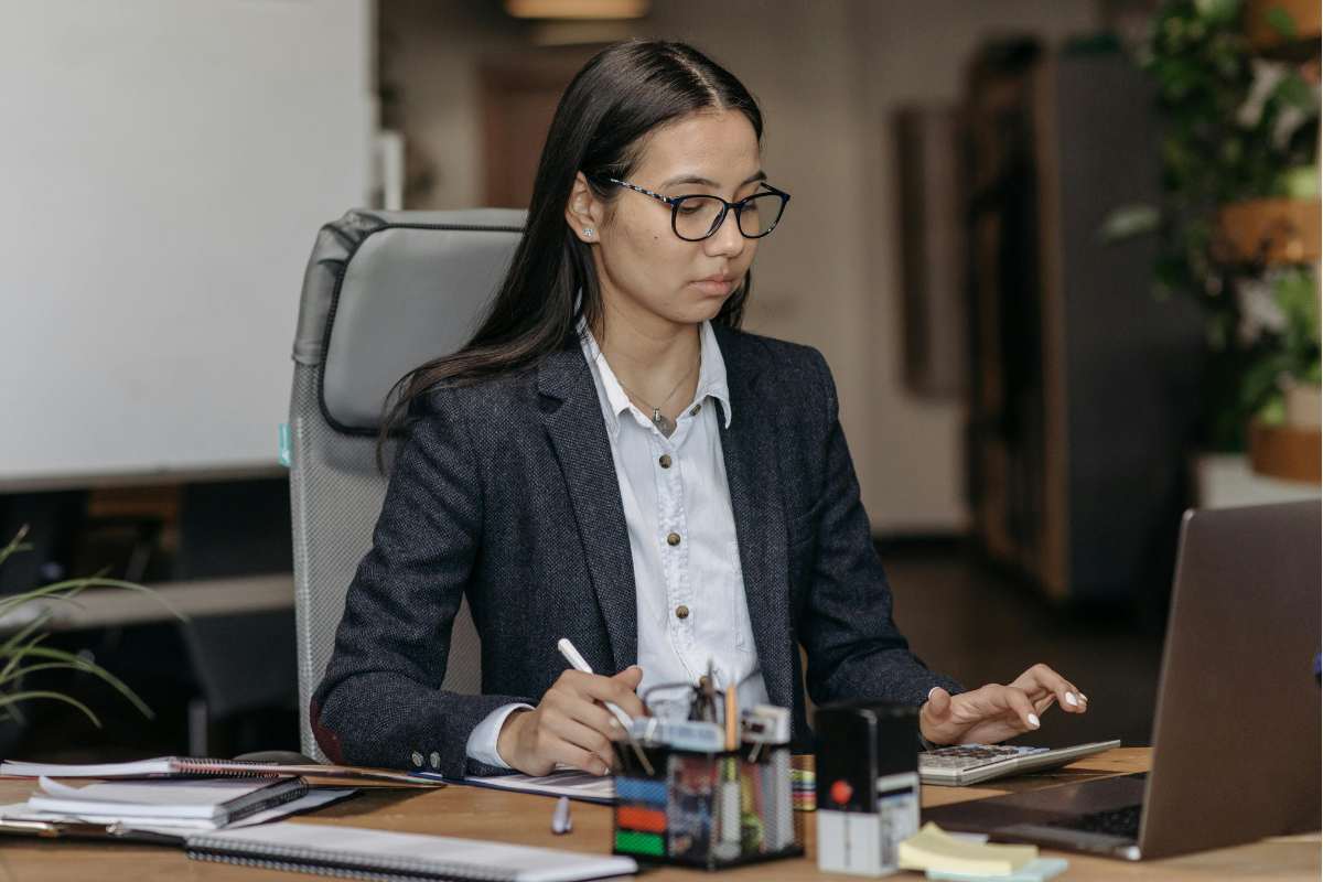Young female clinical auditor nurse using a calculator at an office desk.