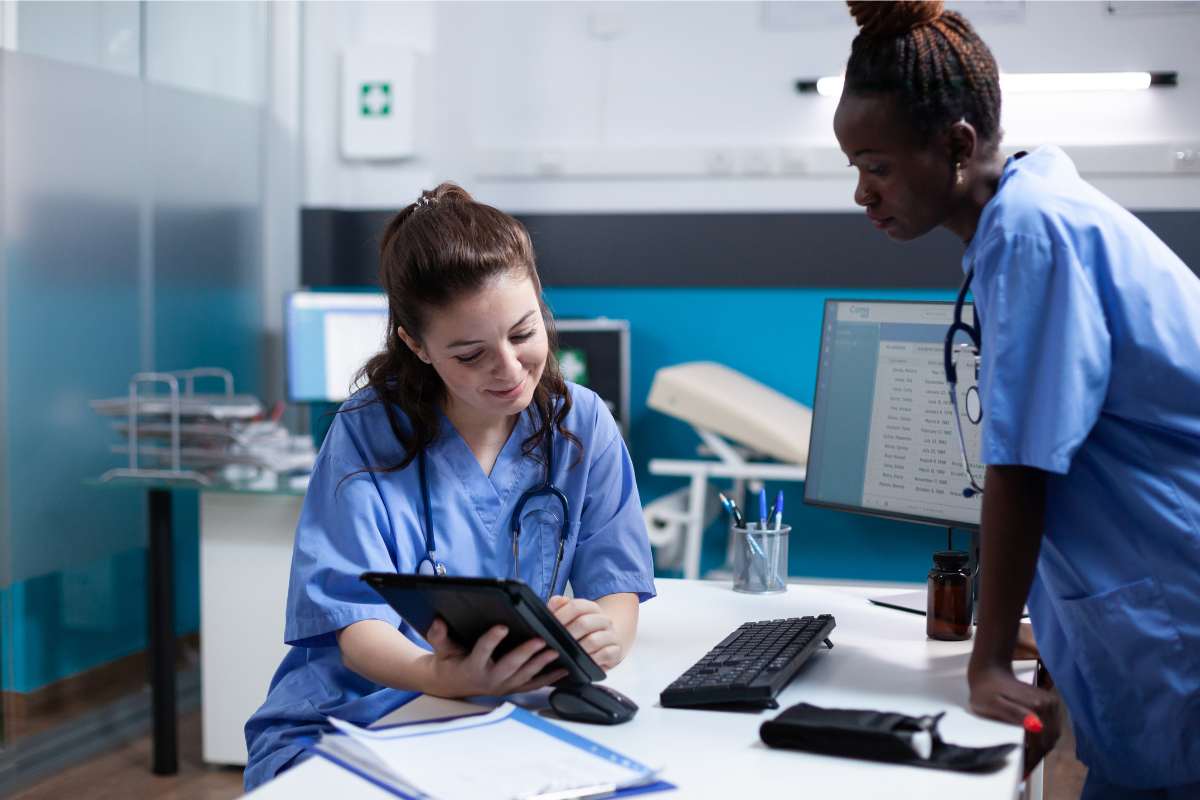 Two nurses in blue scrubs looking at a tablet.