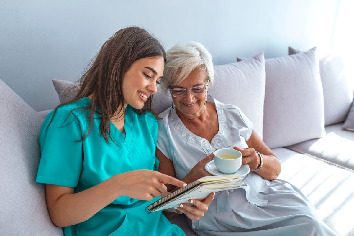 A CNA sits with a nursing home resident who's enjoying a cup of coffee.