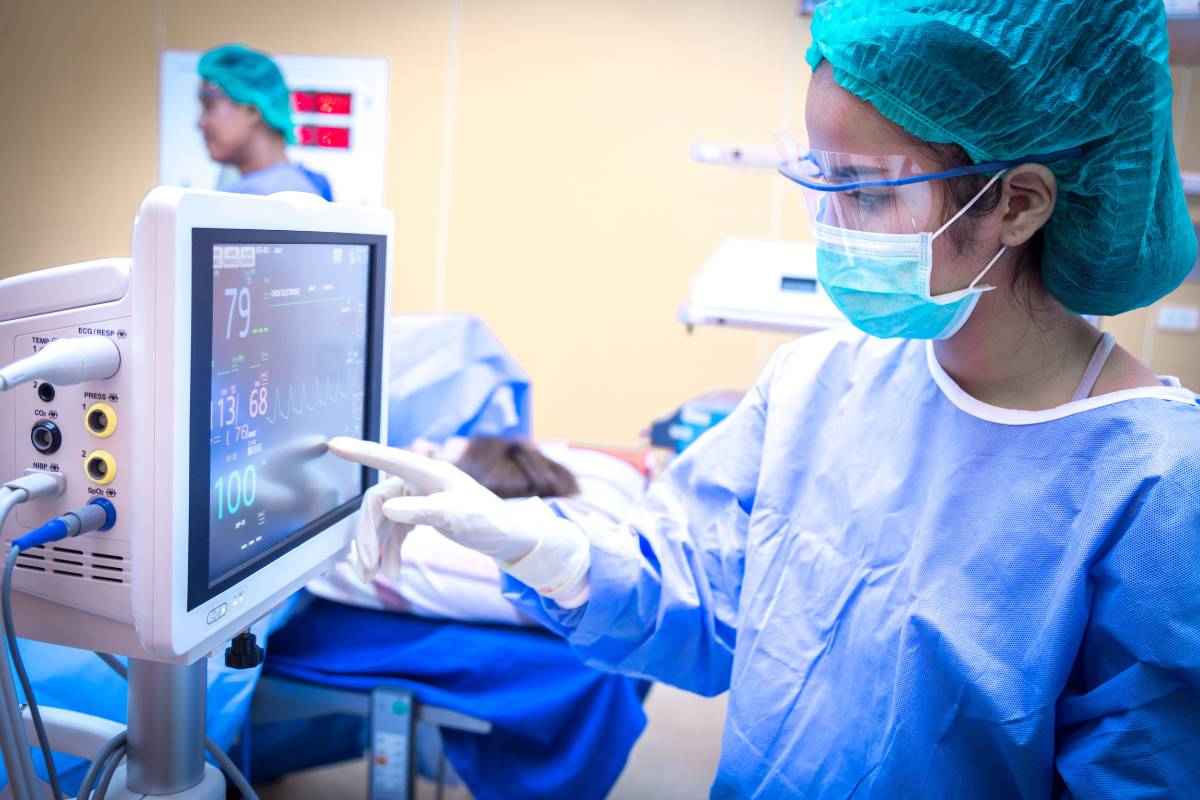 A nurse with CNAMB certification checks a monitor during a surgical procedure.