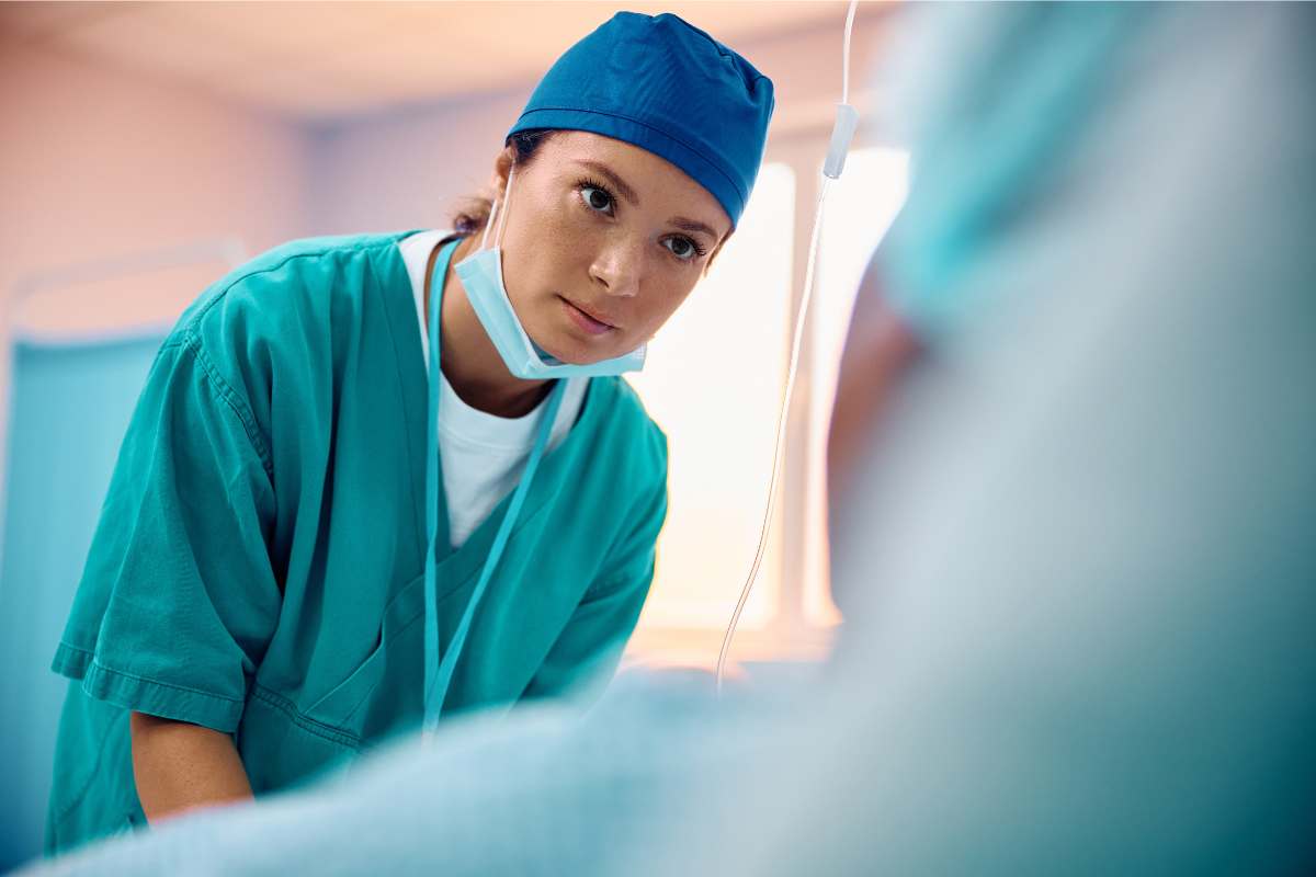 Female critical care technician in scrubs leaning over a patient and listening patiently.