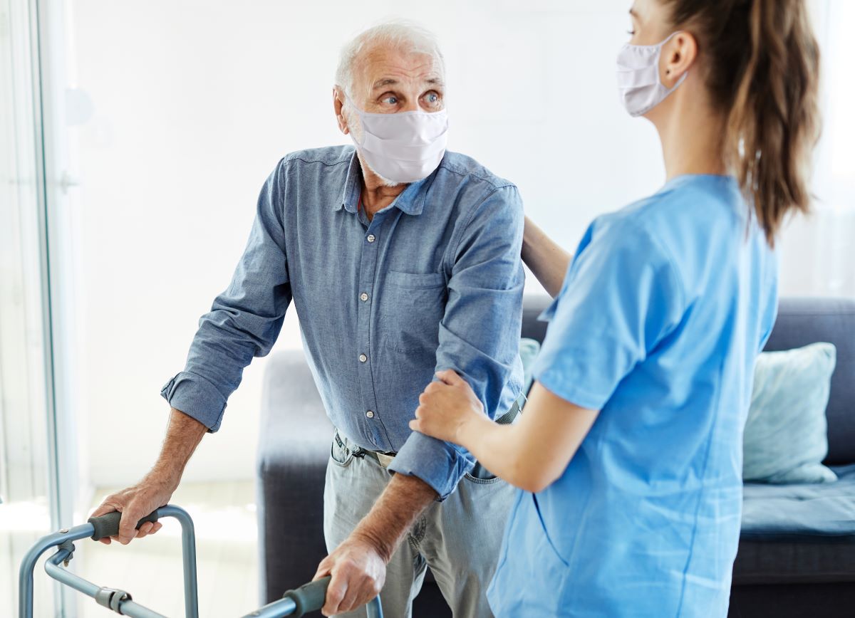 A nurse helps an elderly man safely use a walker.