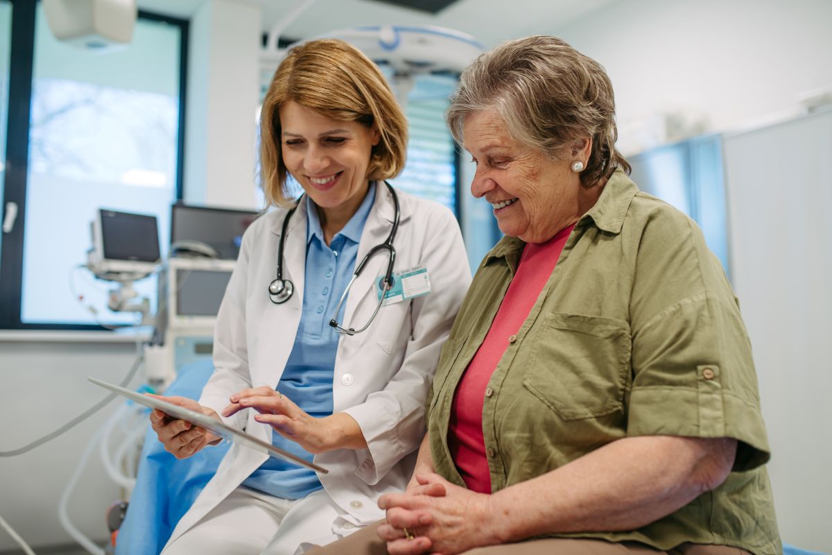A physician sits down next to a patient and discusses her treatment plan with her.