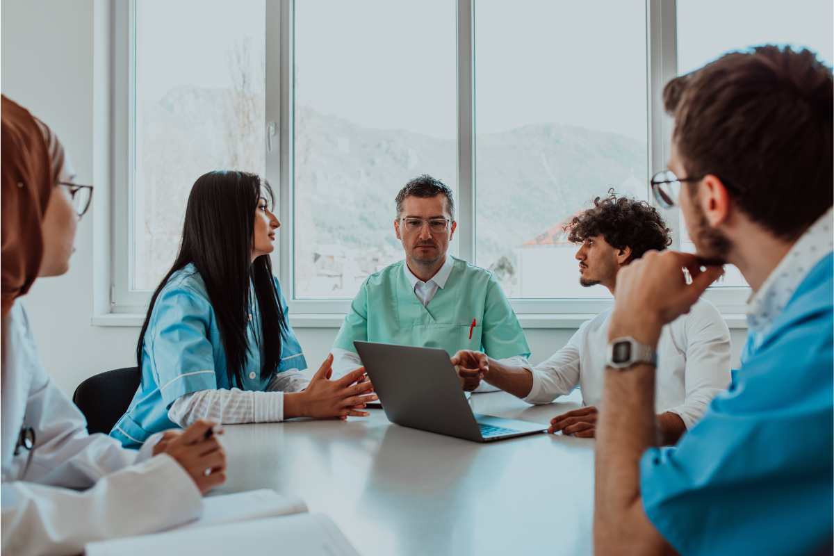 Group of healthcare professionals at the table with a nurse demonstrating his leadership style.
