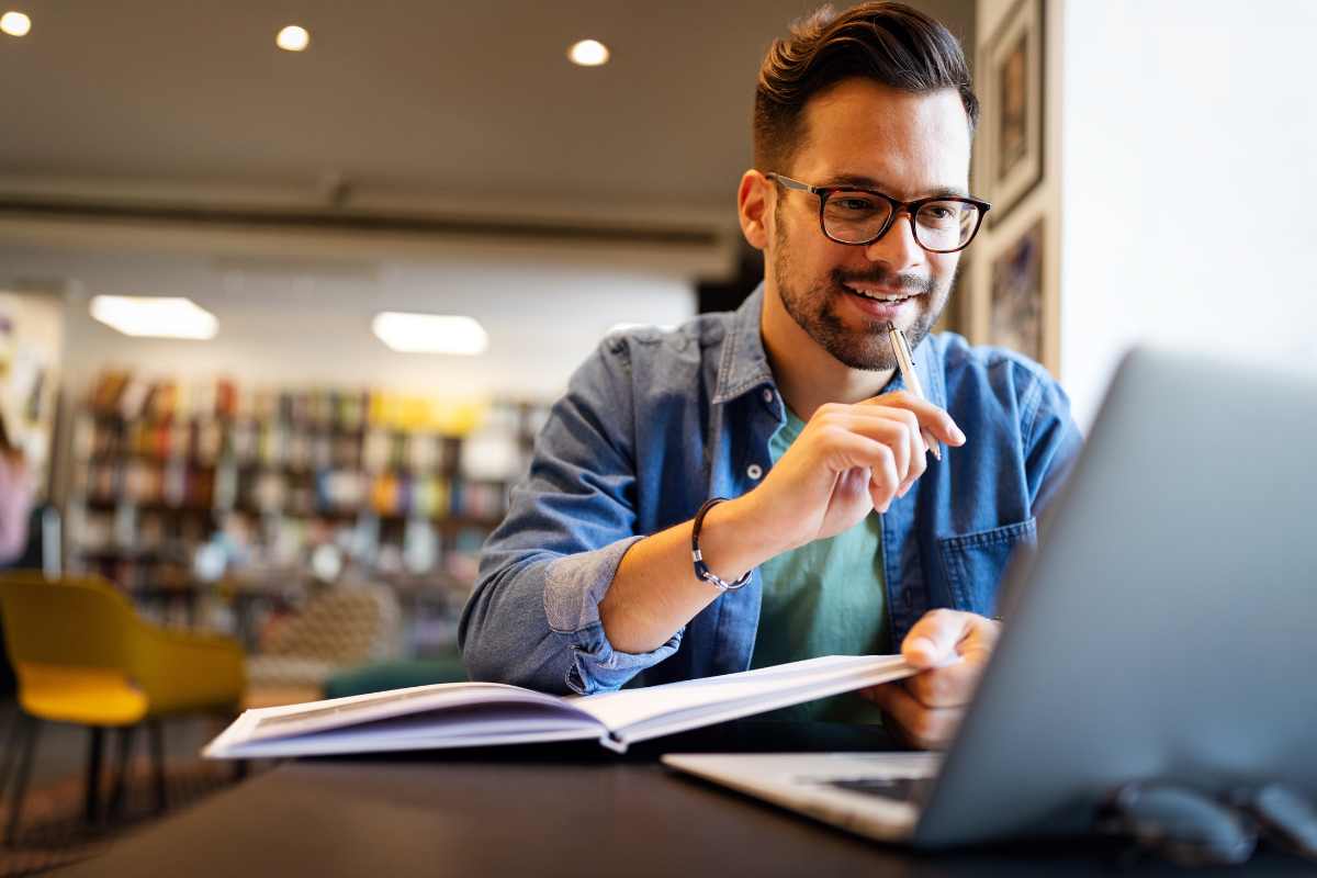 Young man with laptop in a library learning about direct-entry nursing programs.