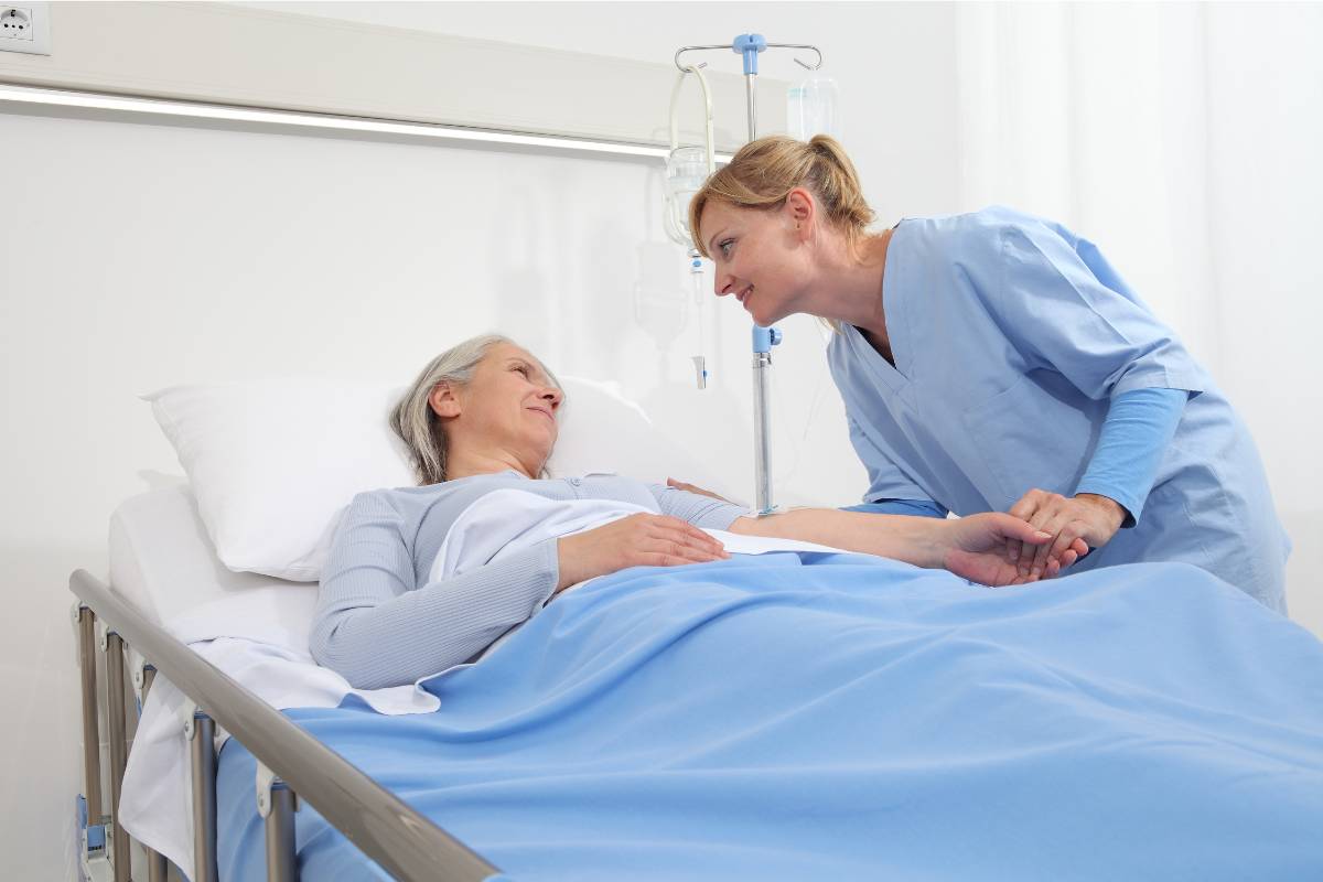 A nurse with ENLS certification assists a patient in a hospital bed.