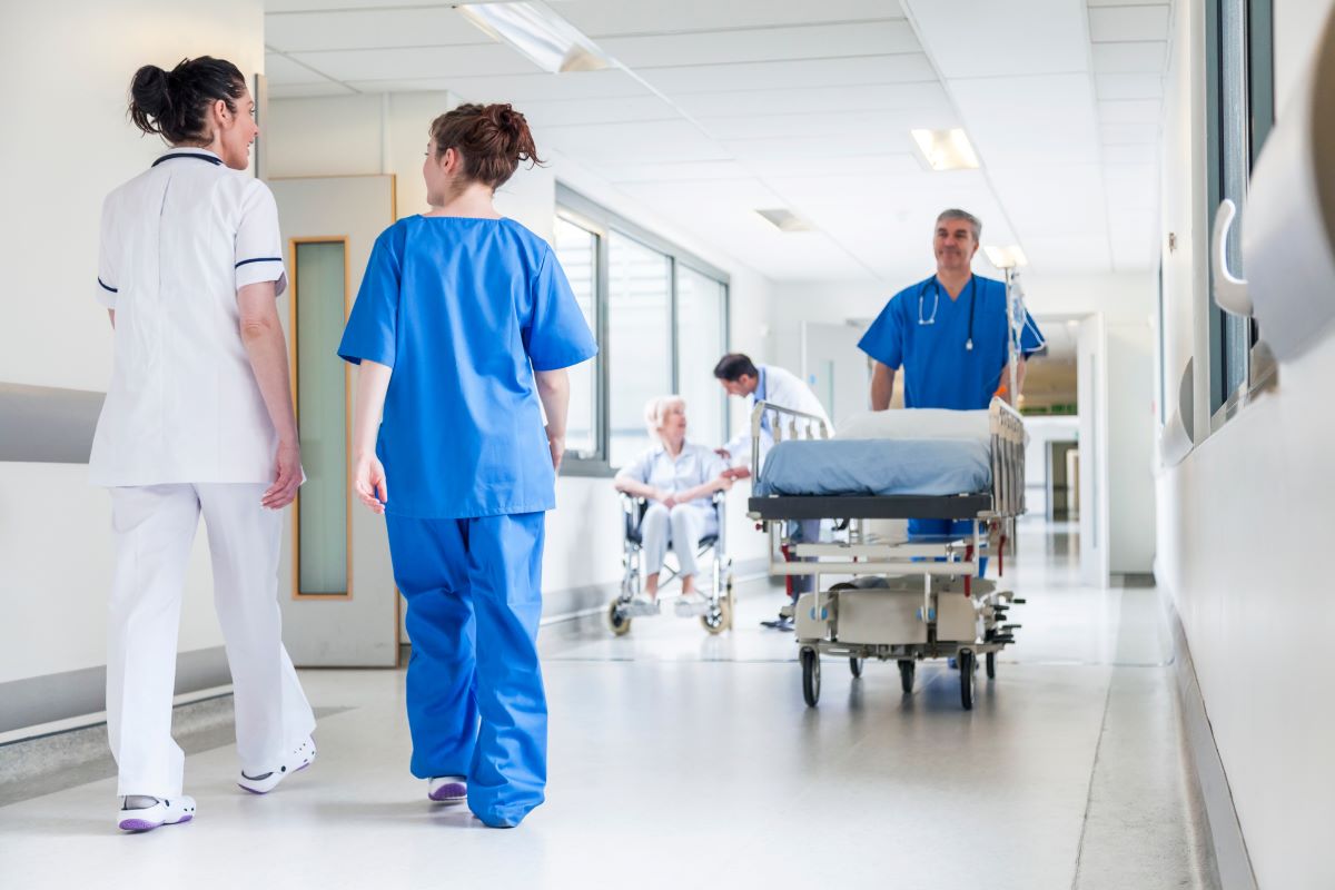 Nurses, with their backs facing the camera, walking down the hallway of a hospital.