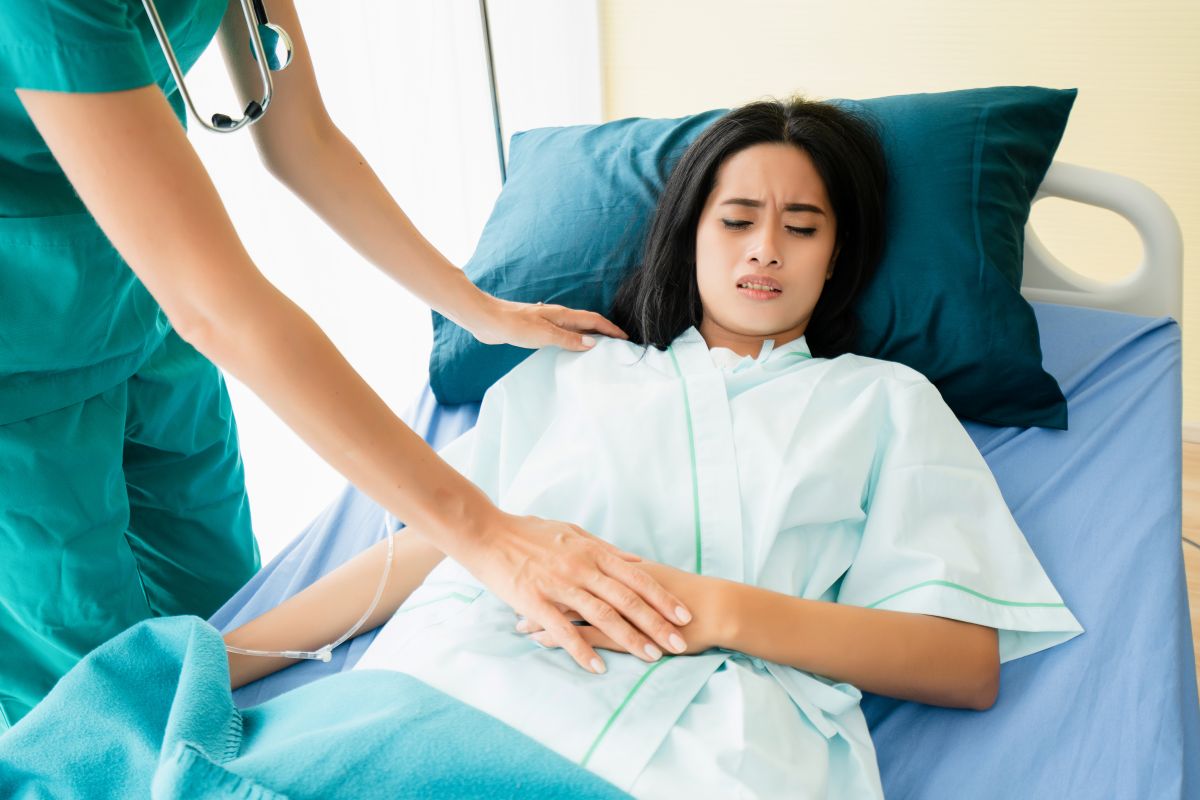 A hospital patient in visible pain gets checked by a nurse.