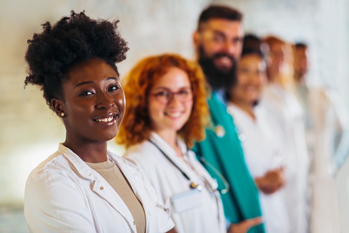 physicians, nurses, and support staff smile for the camera in the hallway of a hospital.