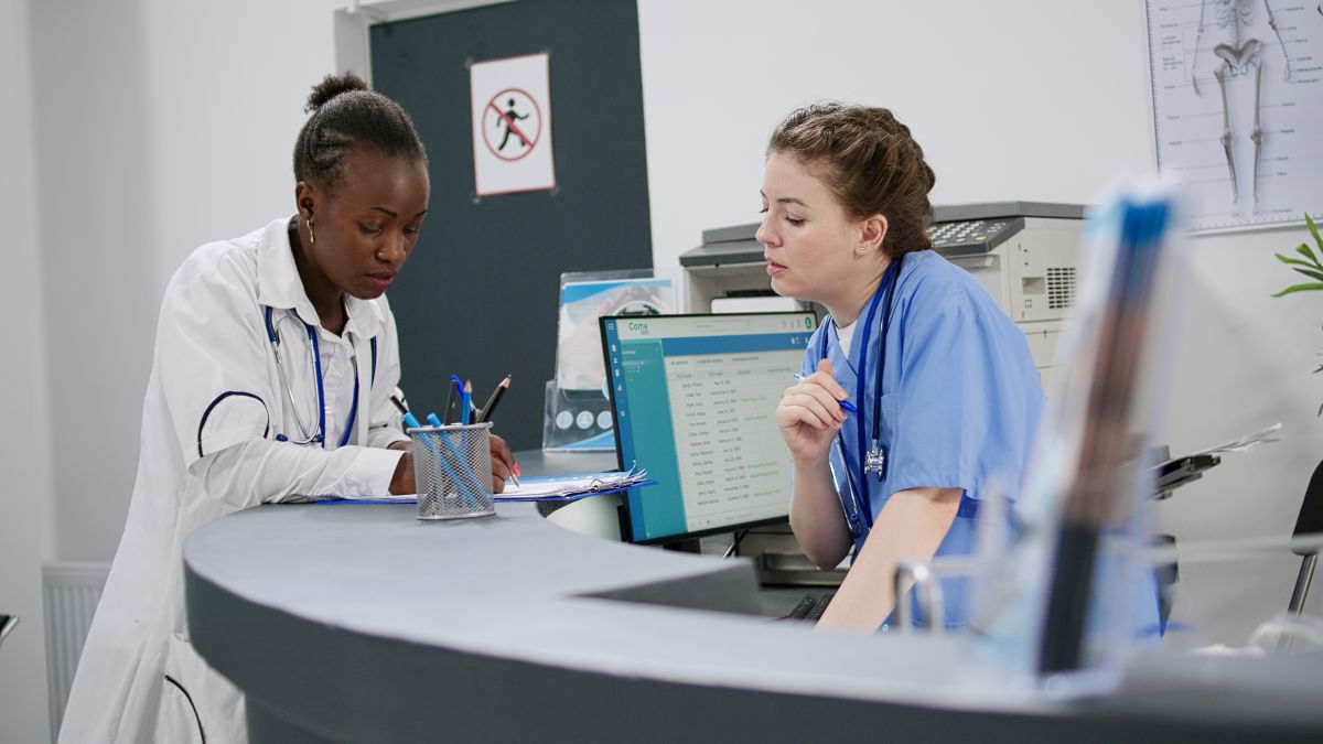 A nurse and a physician have a discussion at a desk.