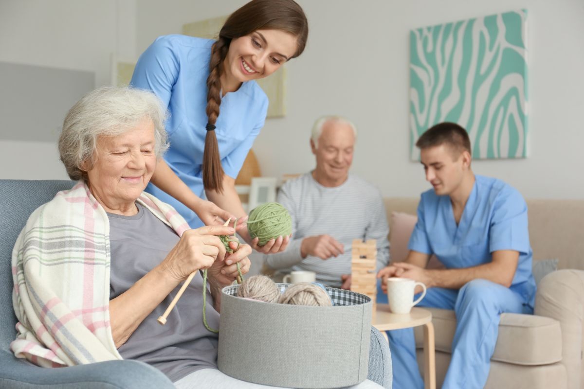 A memory care nurse helps a resident with her knitting.