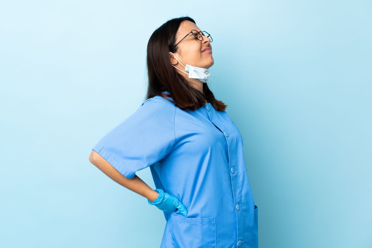 A nurse winces and holds her back, as she deals with lower back pain.