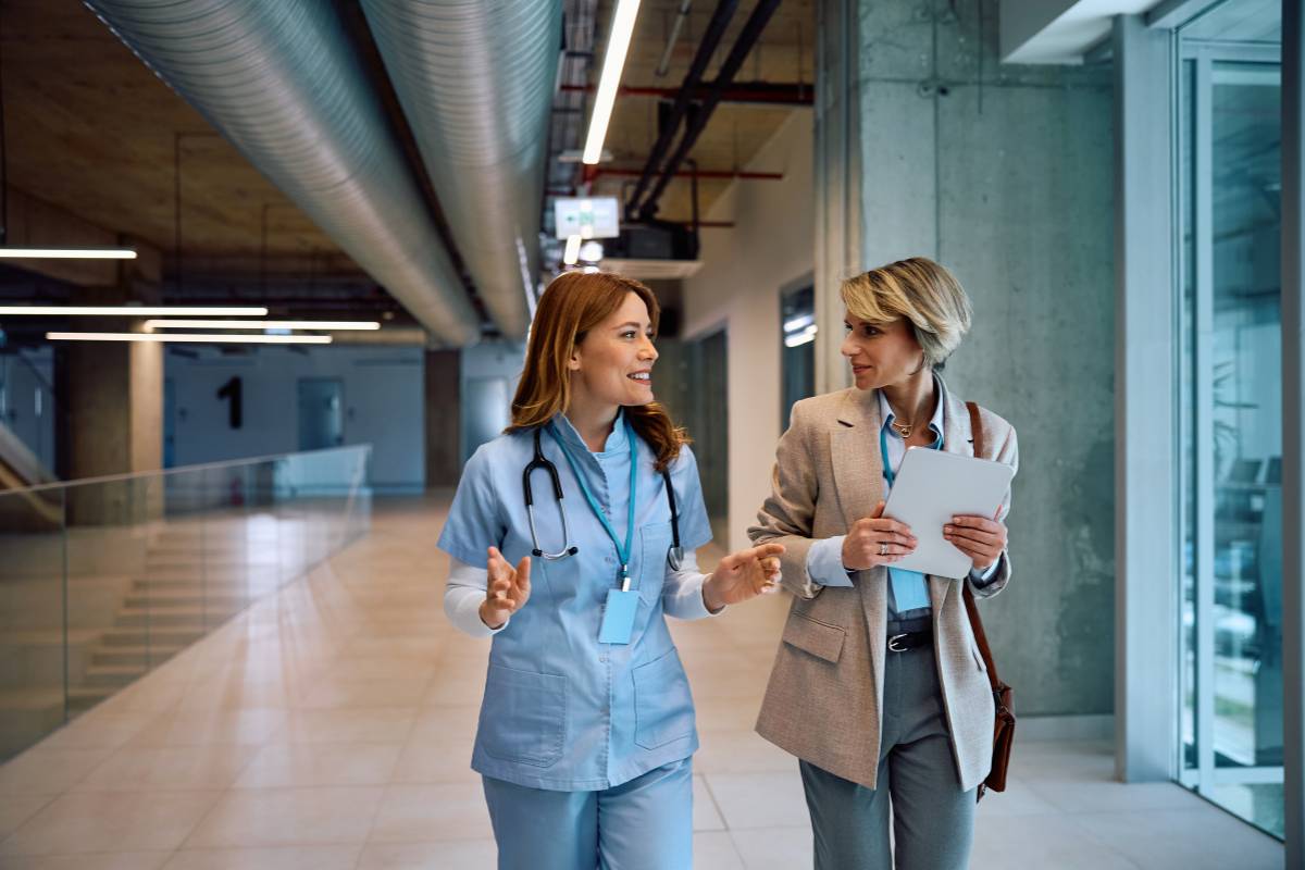 A nurse-engineer team discuss a medical device plan as they walk in a hospital.