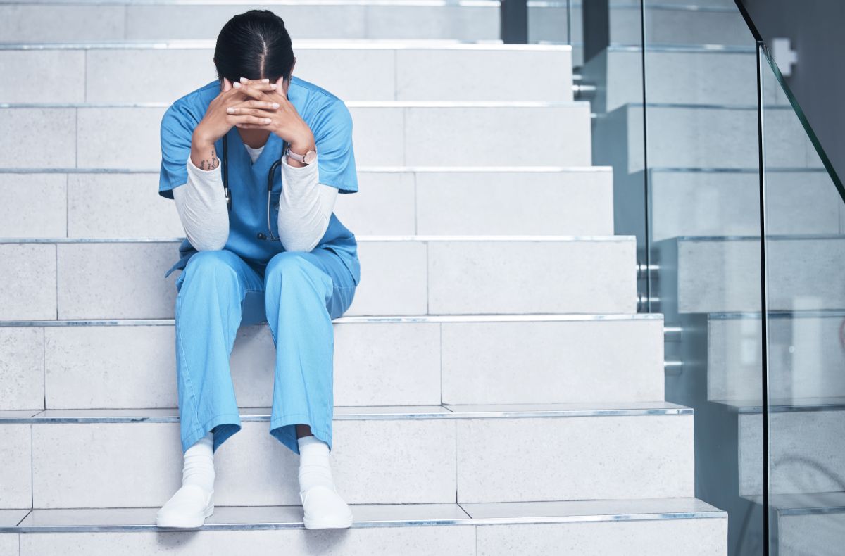 A nurse sitting on the stairs, with her head despondently in her hands.