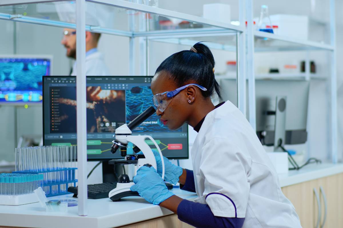 A nurse scientist studies a sample under a microscope.