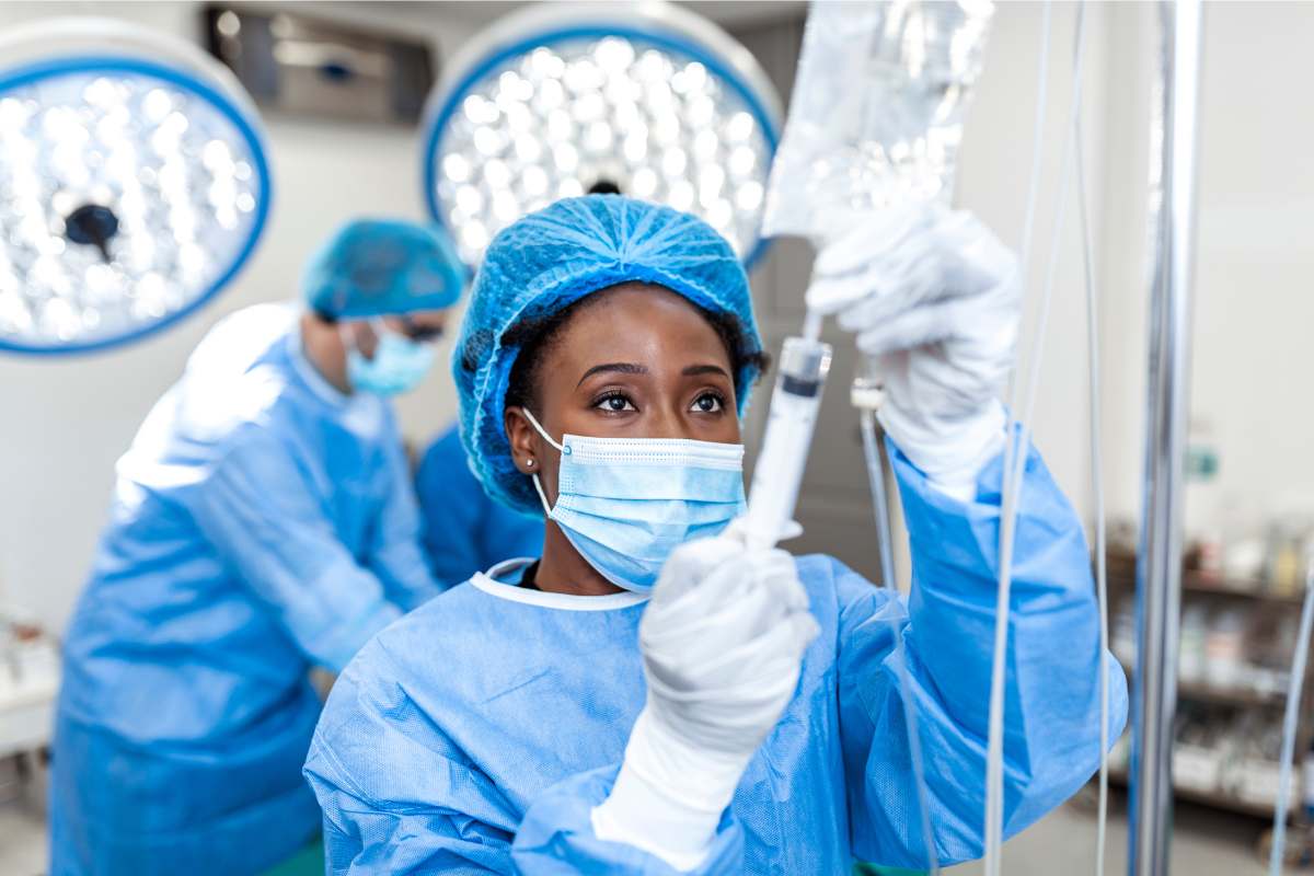 Female African-American surgical nurse administering medication through an IV bag.