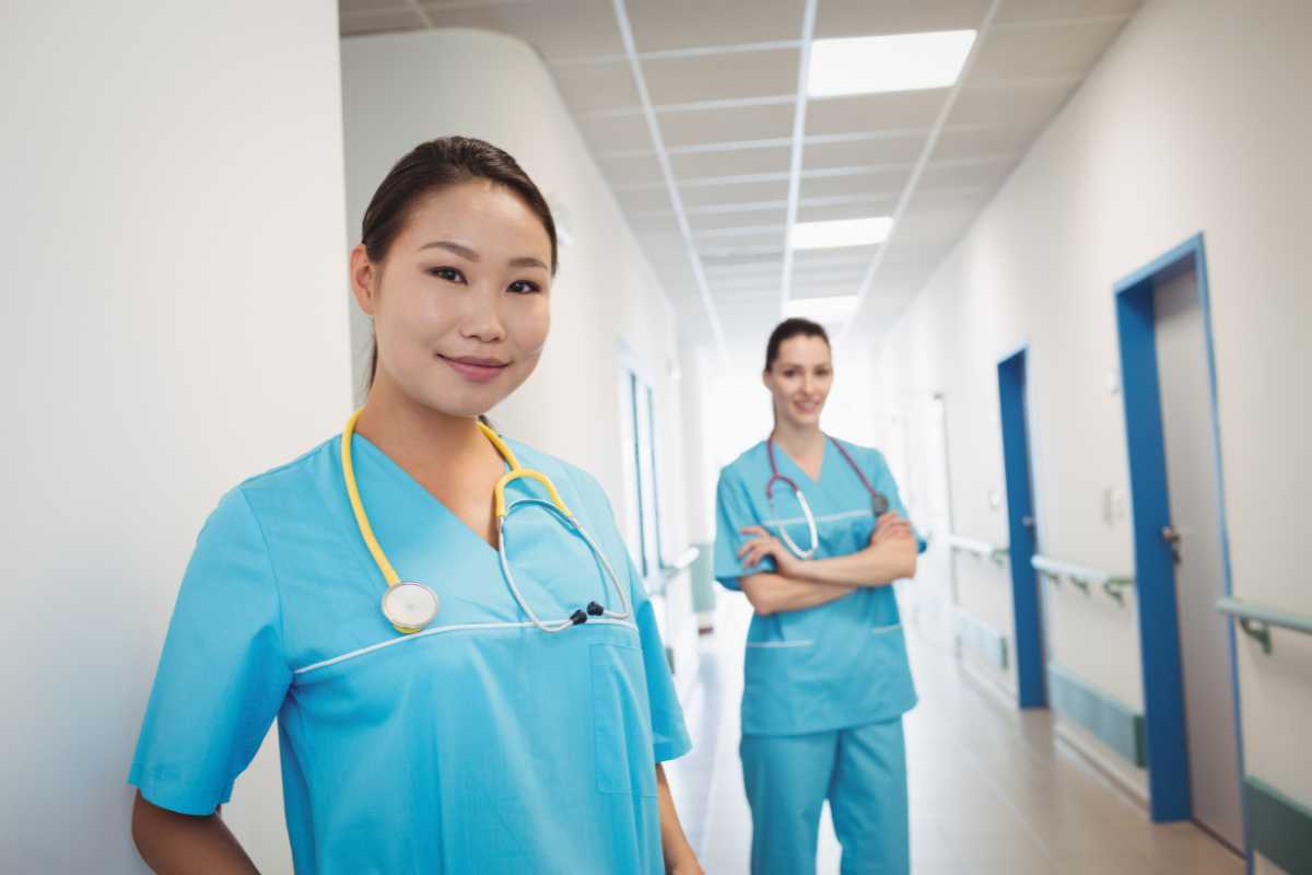 Two nurses in a hospital hallway wearing blue scrubs.